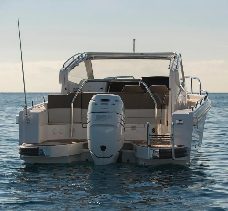 A white motorboat with an outboard engine is anchored in calm waters, facing away from the camera under a clear sky.